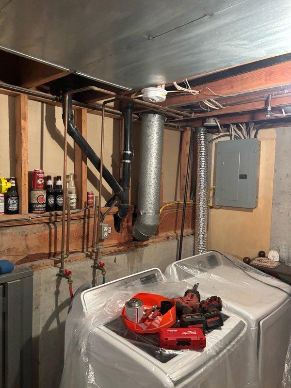 Responded to reported kitchen sink clog and performed diagnostic assessment of drainage system. Upon inspection, accessed plumbing infrastructure in basement utility area beneath kitchen to evaluate drainage lines and identify blockage source. Documented existing plumbing configuration including PVC drainage piping, copper supply lines, and mechanical connections. Prepared work area with catch basin positioned under drainage system to contain water during diagnostic procedures and potential repair work.