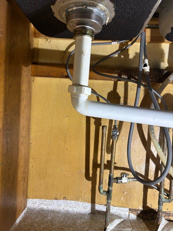 Responded to kitchen sink leak in 50-year-old home. Upon inspection, found deteriorated drain assembly with visible staining and residue buildup around connection points between chrome drain basket and PVC tailpiece. Assessed P-trap configuration and identified leak source at threaded connections where metal components meet plastic piping. Disassembled drain assembly, cleaned all connection surfaces, replaced worn gaskets and seals, and reassembled with proper torque specifications. Verified all connections were secure and tested system under full water flow to confirm leak was eliminated. All plumbing hardware restored to proper working condition with no active leaks detected upon completion.