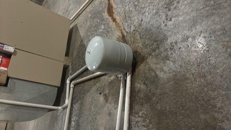 Responded to callback for water heater leaking from bottom in basement. Upon inspection, confirmed active leak requiring bucket placement beneath unit. Assessed pressure tank connections and copper piping with brass fittings for potential sources of water accumulation. Documented existing conditions including PVC drainage system, expansion tank installation, and structural support configuration to determine appropriate repair solution.