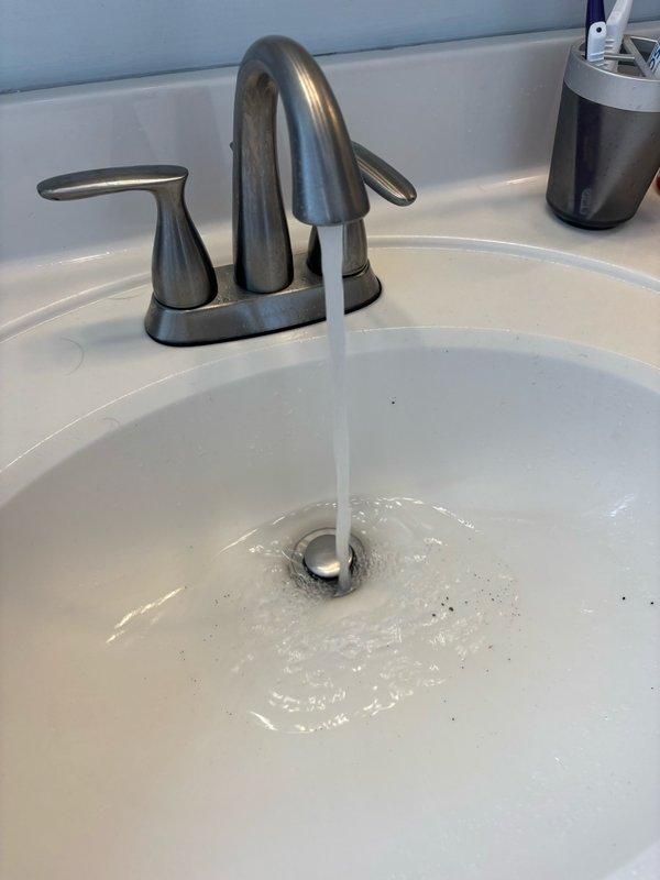 Responded to service call for low water pressure at main bathroom sink and loose faucet handle in kitchen. Inspected bathroom faucet and identified restricted flow due to clogged aerator and debris buildup in supply lines. Disassembled faucet assembly, cleaned aerator screen, and flushed supply lines to restore proper water pressure. Tested flow rate and confirmed adequate pressure restoration. Proceeded to kitchen where faucet handle was found to be loose due to worn mounting hardware. Tightened handle set screw and verified secure operation of handle mechanism. Documented pre-repair and post-repair conditions with photographs showing water flow at bathroom sink. All fixtures tested and left in proper working order.