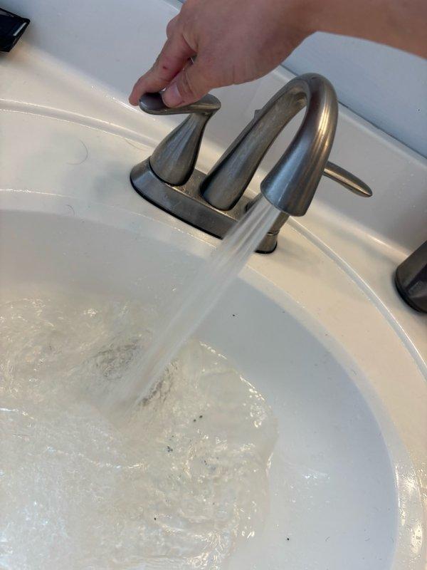Responded to service call for low water pressure at main bathroom sink and loose faucet handle in kitchen. Inspected bathroom faucet and identified restricted flow due to clogged aerator and debris buildup in supply lines. Disassembled faucet assembly, cleaned aerator screen, and flushed supply lines to restore proper water pressure. Tested flow rate and confirmed adequate pressure restoration. Proceeded to kitchen where faucet handle was found to be loose due to worn mounting hardware. Tightened handle set screw and verified secure operation of handle mechanism. Documented pre-repair and post-repair conditions with photographs showing water flow at bathroom sink. All fixtures tested and left in proper working order.