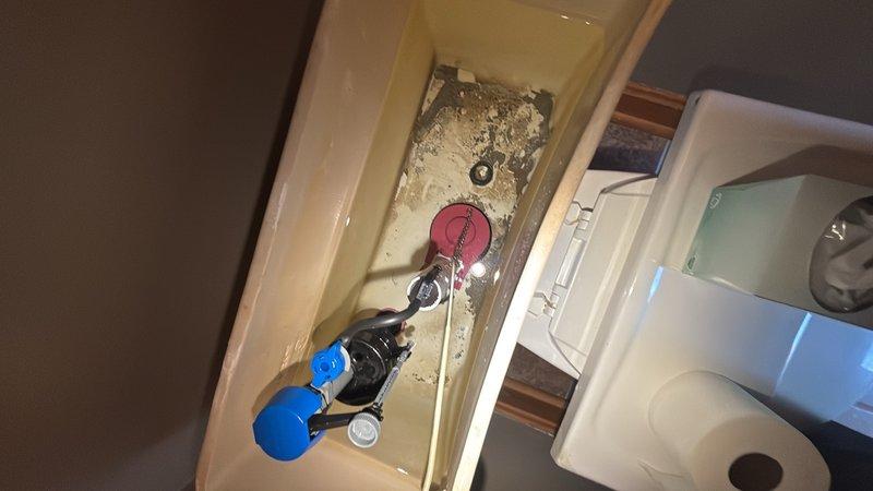 Responded to reported water leak originating from bathroom and penetrating into basement below kitchen area. Upon investigation, inspected toilet tank components and identified deteriorated flush mechanism with visible mineral buildup and sediment accumulation. Documented internal tank condition showing worn flapper valve, fill valve assembly, and significant hard water deposits on porcelain surfaces indicating potential seal failure as leak source.