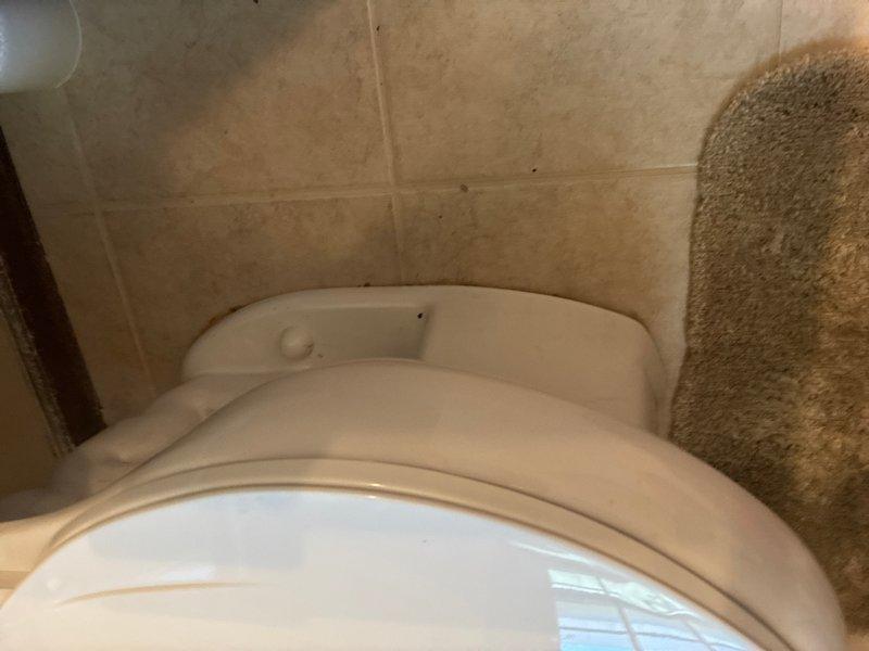 Responded to water leak complaint with visible water damage on kitchen ceiling directly below upstairs bathroom. Upon inspection, identified toilet as source of leak with evidence of water staining and discoloration at base connection point where fixture meets floor. Documented conditions showing compromised seal at toilet base with visible moisture intrusion through ceiling below. Recommended immediate repair or replacement of wax ring seal and proper resetting of toilet to prevent continued water damage to ceiling and underlying structure.
