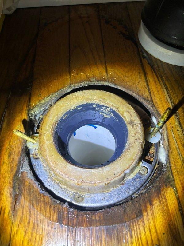Responded to reported toilet leak in bathroom. Upon inspection, discovered active water seepage at the base of the toilet where it meets the wooden floor, with visible moisture damage to surrounding wood planks. Removed toilet from floor flange to assess source of leak. Found compromised wax ring seal allowing water to escape during flushing. Removed failed wax ring, cleaned toilet flange and horn, and installed new wax ring seal. Reinstalled toilet, ensuring proper alignment with flange bolts and secure mounting to floor. Tested flush operation multiple times to verify leak was eliminated and seal is functioning properly.