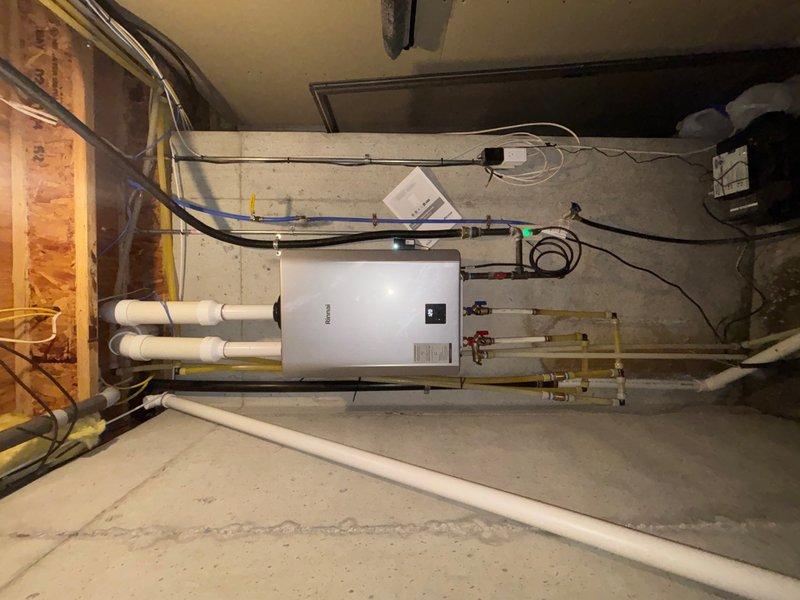 Successfully completed tankless water heater replacement in basement utility area. Removed existing water heating system and installed new wall-mounted tankless unit on concrete block wall with proper venting through white PVC exhaust and intake piping. Connected gas supply line, installed shutoff valves on water supply lines, and completed electrical wiring with conduit to dedicated circuit. System tested and calibrated to proper operating temperature, with unit displaying normal operational parameters upon completion.