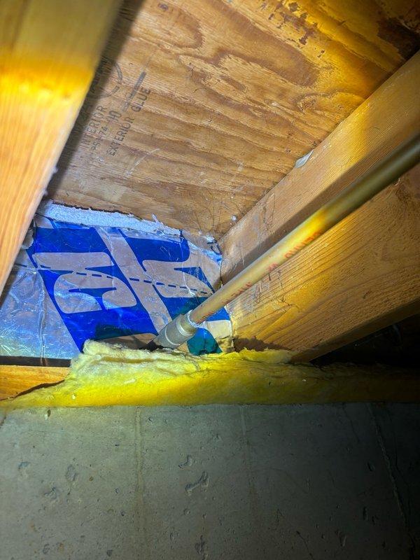 Responded to service call for exterior hose bibb that was difficult to operate and experiencing leakage issues when shutting off. Accessed the outdoor spigot from interior crawl space to diagnose the problem. Upon inspection, found the supply line and shutoff valve assembly in the basement area beneath the exterior wall penetration. The copper supply piping and associated connections showed signs of age and wear. Evaluated the valve mechanism and determined the root cause of the operational difficulty and leaking condition. Documented the existing installation with photographic evidence showing the supply line routing through floor joists with surrounding insulation, as well as the pipe penetration through the foundation wall. The images captured the current state of the plumbing assembly, insulation placement, and structural elements for reference. Provided assessment of necessary repairs to restore proper function and eliminate the leak when closing the valve.