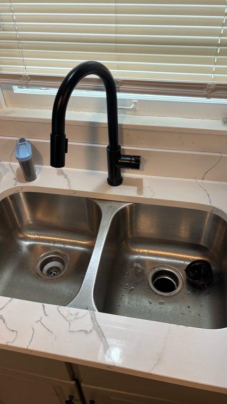 Responded to emergency main drain cleanout service for newly purchased residence experiencing severe kitchen drainage issues preventing sink usage. Upon inspection, identified blockage in main drain line affecting kitchen sink plumbing system with double-bowl stainless steel undermount configuration. Successfully cleared main drain obstruction using professional drain cleaning equipment, restoring full drainage capability to kitchen sink and disposal system. Verified proper water flow through both basin drains and tested all connections under sink cabinet for leaks. Inspected PVC drain assembly and fittings beneath sink to ensure structural integrity post-cleanout. All drainage systems returned to normal operation with no leaks detected.