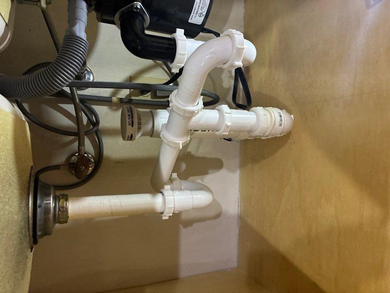 Responded to reported water leak under kitchen sink near garbage disposal drain assembly. Upon inspection, identified leak originating from drain connection point between disposal unit and PVC P-trap assembly. Tightened compression fittings at disposal discharge elbow and verified all threaded connections throughout the drain system. Inspected corrugated dishwasher drain hose connection to disposal inlet port and confirmed secure attachment. Tested system by running water through disposal and sink drain while monitoring all connection points for leakage. Verified proper drainage flow through P-trap assembly to wall drain. No further leaks detected upon completion of repair.