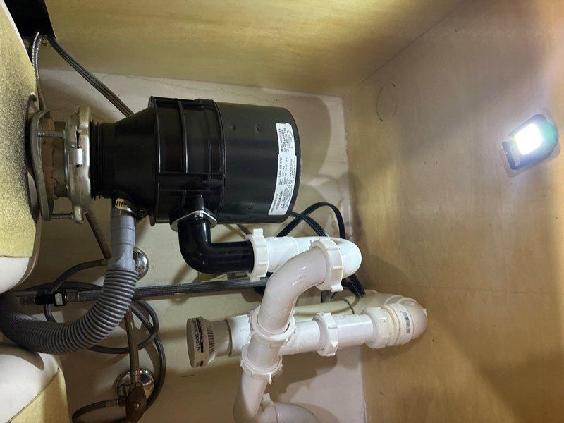 Responded to reported water leak under kitchen sink near garbage disposal drain assembly. Upon inspection, identified leak originating from drain connection point between disposal unit and PVC P-trap assembly. Tightened compression fittings at disposal discharge elbow and verified all threaded connections throughout the drain system. Inspected corrugated dishwasher drain hose connection to disposal inlet port and confirmed secure attachment. Tested system by running water through disposal and sink drain while monitoring all connection points for leakage. Verified proper drainage flow through P-trap assembly to wall drain. No further leaks detected upon completion of repair.