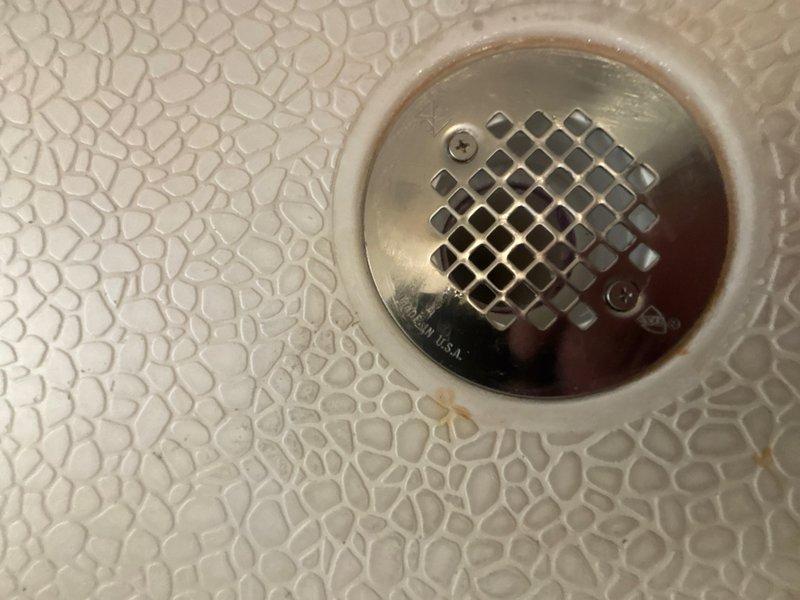 Successfully replaced a defective PVC shower drain assembly with a new chrome-plated drain cover featuring a diamond-pattern perforated grate secured with stainless steel screws. The replacement drain was properly installed within the existing white ceramic drain ring on the textured non-slip shower floor surface, restoring full drainage functionality to the shower unit.