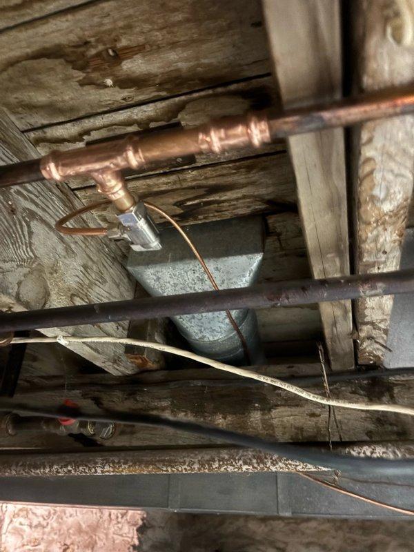 Responded to emergency call for active water leak in basement of century-old home. Upon arrival, found hot water line had been accidentally pierced during recent AC humidifier installation, causing water to spray throughout the basement area. Homeowner had temporarily stopped the leak by shutting off hot water supply at the water heater. Inspected the damaged copper supply line running through the basement ceiling joists and identified the puncture point where the line had been compromised during the previous week's HVAC work. Assessed the surrounding plumbing infrastructure, including multiple copper pipes and connections in the unfinished basement space. Repaired the pierced hot water line by cutting out the damaged section and installing new copper piping with properly soldered joints and fittings. Restored water supply and pressure tested all connections to ensure no additional leaks were present. Verified proper operation of the hot water system and confirmed the humidifier supply