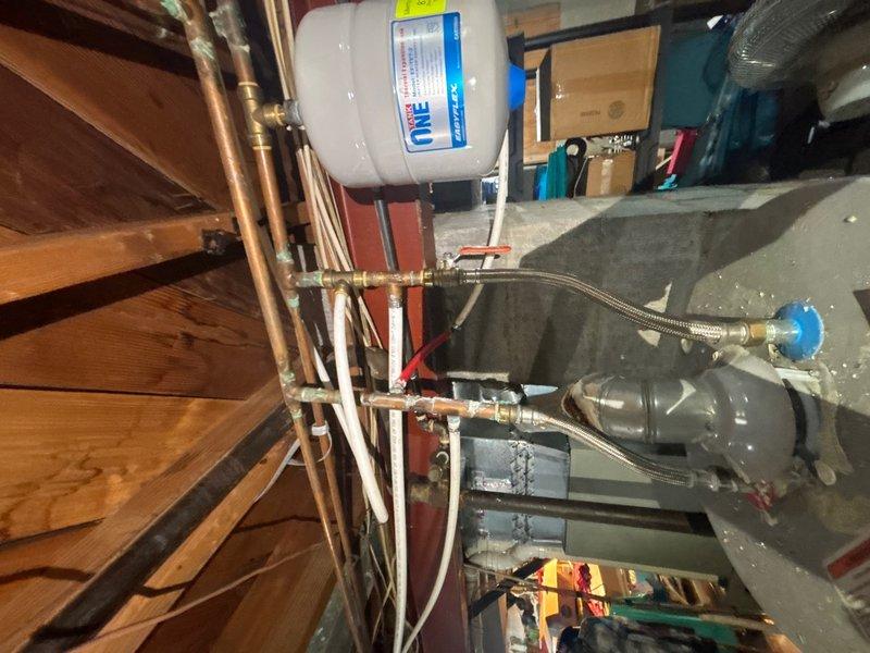 Responded to reported water intrusion in basement occurring during rain events. Conducted thorough leak location inspection of basement area, identifying significant moisture damage and standing water accumulation in corner section near foundation walls. Documented extensive water staining, discoloration, and deterioration on concrete block walls indicating chronic water infiltration issues. Inspected plumbing system components including expansion tank, pressure tank, copper piping, brass fittings, and flexible connector hoses to rule out internal plumbing leaks as source. Determined water intrusion pattern consistent with exterior foundation leak rather than plumbing system failure. Photographed affected areas showing pooled water, wall deterioration, mold growth patterns, and existing drainage components. Advised that repairs would be required to address foundation waterproofing and proper exterior drainage to resolve recurring moisture problem.