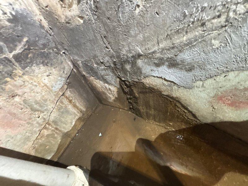 Responded to reported water intrusion in basement occurring during rain events. Conducted thorough leak location inspection of basement area, identifying significant moisture damage and standing water accumulation in corner section near foundation walls. Documented extensive water staining, discoloration, and deterioration on concrete block walls indicating chronic water infiltration issues. Inspected plumbing system components including expansion tank, pressure tank, copper piping, brass fittings, and flexible connector hoses to rule out internal plumbing leaks as source. Determined water intrusion pattern consistent with exterior foundation leak rather than plumbing system failure. Photographed affected areas showing pooled water, wall deterioration, mold growth patterns, and existing drainage components. Advised that repairs would be required to address foundation waterproofing and proper exterior drainage to resolve recurring moisture problem.