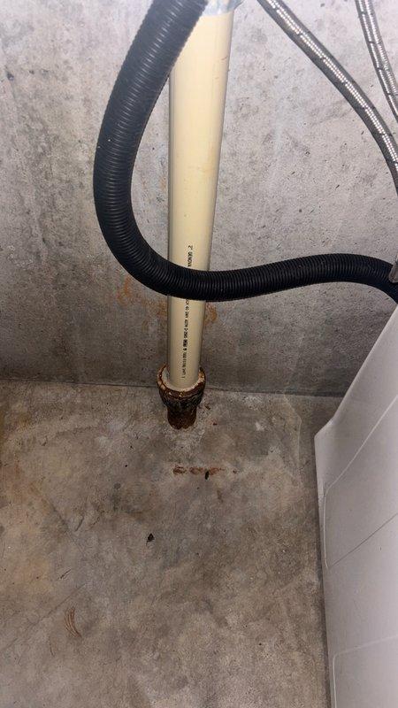 Responded to service call for leaking washer drain line connection. Upon inspection, identified corroded metal drain pipe fitting where PVC standpipe transitions to cast iron drainage system at floor level. The metal coupling showed active rust deterioration causing water seepage at the joint connection. Documented existing plumbing configuration including PVC standpipe with flexible drain hose connection and provided estimate for replacement of corroded metal fitting with appropriate corrosion-resistant materials to restore proper drainage function and eliminate leak.
