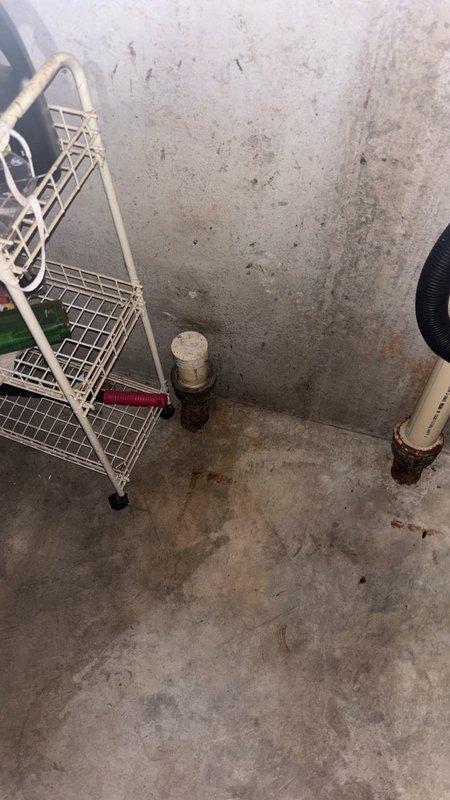 Responded to service call for leaking washer drain line connection. Upon inspection, identified corroded metal drain pipe fitting where PVC standpipe transitions to cast iron drainage system at floor level. The metal coupling showed active rust deterioration causing water seepage at the joint connection. Documented existing plumbing configuration including PVC standpipe with flexible drain hose connection and provided estimate for replacement of corroded metal fitting with appropriate corrosion-resistant materials to restore proper drainage function and eliminate leak.