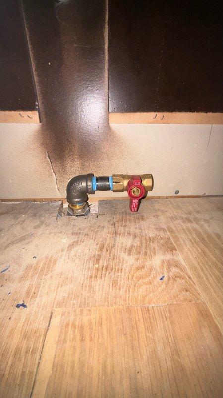 Relocated gas line supply for residential gas range installation. Installed black iron pipe with elbow fitting, brass connectors, and red-handled shut-off valve to new location. Created access opening in flooring near kitchen island to accommodate new gas line routing. All connections properly secured with appropriate fittings and valve installed for safe gas flow control to appliance.