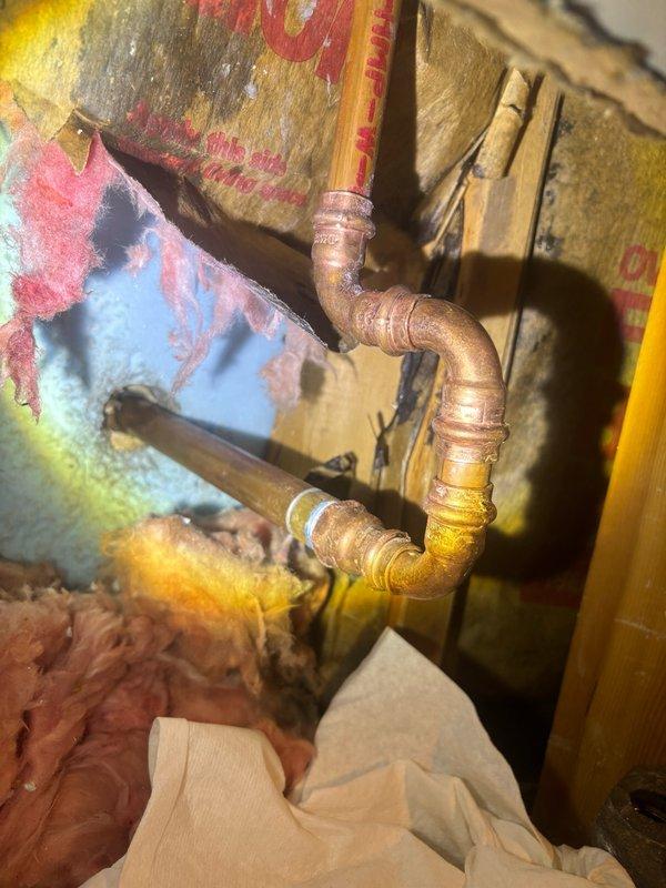 Responded to a leak locate service call where the hose bib was initially leaking externally and was shut off by HVAC personnel, resulting in water leaking inside the wall cavity. Upon inspection, accessed the interior wall space and located the affected copper piping assembly between wall studs. The copper pipes showed significant age-related oxidation and patina, indicating an older plumbing installation. Documented the condition of the piping system, including soldered joints and fittings, to identify the source of the interior leak caused by shutting off the exterior hose bib valve.