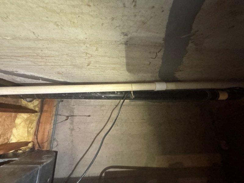 Conducted comprehensive assessment of existing sump pump system in basement crawl space area. Inspected drainage piping configuration, including white PVC discharge lines and connections at floor joist level. Evaluated current pump location, discharge routing through ceiling joists, and identified elbow joint connections in the drainage system. Examined structural conditions of surrounding area, noting insulation placement and accessibility for potential installation or replacement work. Documented existing plumbing infrastructure and provided detailed estimate for sump pump service requirements.