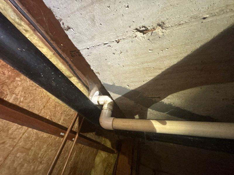 Conducted comprehensive assessment of existing sump pump system in basement crawl space area. Inspected drainage piping configuration, including white PVC discharge lines and connections at floor joist level. Evaluated current pump location, discharge routing through ceiling joists, and identified elbow joint connections in the drainage system. Examined structural conditions of surrounding area, noting insulation placement and accessibility for potential installation or replacement work. Documented existing plumbing infrastructure and provided detailed estimate for sump pump service requirements.