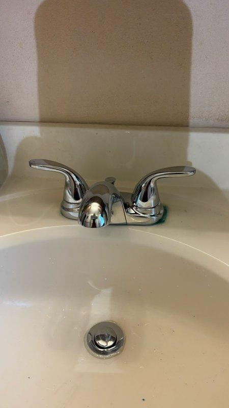 Completed installation of chrome two-handle bathroom faucet on main level. The faucet was mounted to cream-colored countertop with matching basin and pop-up drain assembly. During installation, addressed underlying plumbing issues including disconnecting and servicing the P-trap assembly, which required clearing debris and sediment buildup. Wall-mounted drain connections were inspected and reassembled to ensure proper drainage function. All fixtures tested and confirmed operational upon completion.