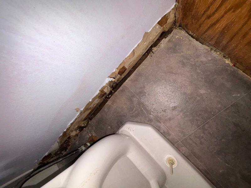 Responded to service call for possible water leak near toilet in 1990s-era home. Upon inspection, identified significant moisture damage and deterioration along wall-to-floor junction near toilet area, with visible water damage to baseboard, drywall, and subflooring materials. Documented extensive damage with photographs showing compromised wall structure, exposed substrate, and dark discoloration consistent with prolonged water intrusion. Leak source located at toilet base connection where deteriorated wax ring and compromised flange seal allowed water to escape during flushing cycles. Recommended immediate repairs including toilet removal, replacement of wax ring and flange, and remediation of water-damaged drywall, baseboard, and subfloor materials before reinstallation.