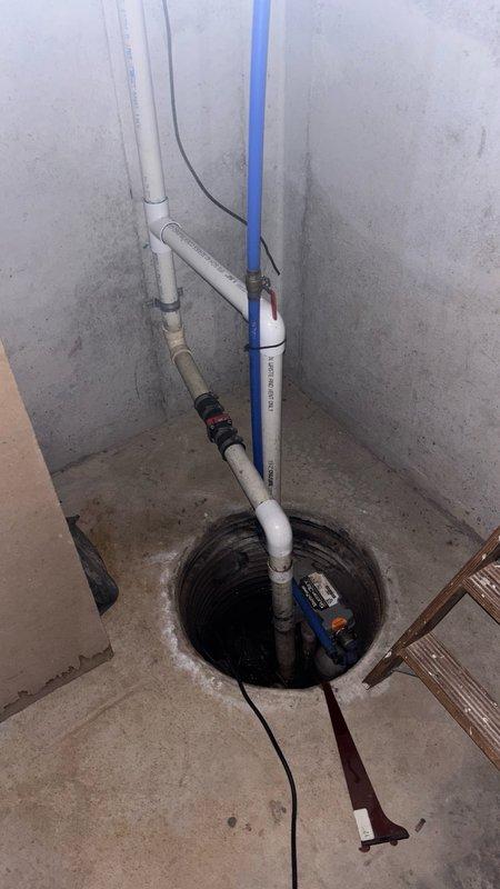 Responded to callback for banging noise issue in basement sump pump system. Upon arrival, inspected sump pump basin, discharge piping, and check valve assembly. Customer had identified the source of noise as being connected to the sump pump exit pipe. Examined white PVC discharge pipe configuration, check valve installation, and verified proper pump operation. Documented existing conditions with photos showing sump pump basin with submersible pump, electrical connections, discharge piping with check valve, and overall plumbing configuration. Verified pump cycling and discharge flow through exit piping system.