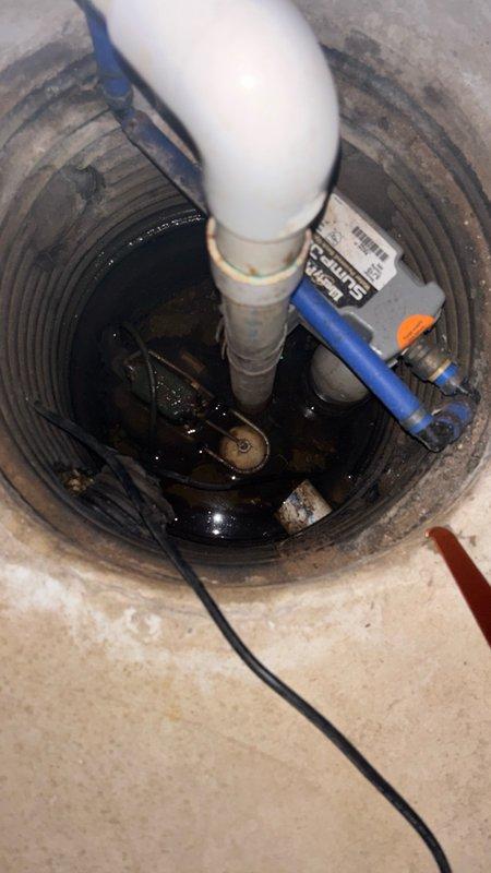 Responded to callback for banging noise issue in basement sump pump system. Upon arrival, inspected sump pump basin, discharge piping, and check valve assembly. Customer had identified the source of noise as being connected to the sump pump exit pipe. Examined white PVC discharge pipe configuration, check valve installation, and verified proper pump operation. Documented existing conditions with photos showing sump pump basin with submersible pump, electrical connections, discharge piping with check valve, and overall plumbing configuration. Verified pump cycling and discharge flow through exit piping system.