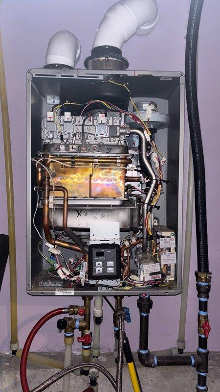 Responded to service call for Rinnai RUC80 tankless water heater experiencing intermittent hot water failure. Upon arrival, unit was operational following customer-initiated reset, but diagnostic history revealed Code 10 (air supply/combustion issue), Code 11 (ignition failure), and Code 57 (high limit switch/bimetal switch activation). Performed comprehensive system inspection of unit located in ground floor laundry/utility closet. Visually inspected external intake and exhaust vents on building exterior, confirming both PVC terminations were clear of obstructions. Removed front service panel to examine internal components, heat exchanger assembly, combustion chamber, and control board. Observed heat exchanger condition and verified flame sensor operation. Checked gas supply connections, water inlet/outlet plumbing, and all electrical connections for proper installation and condition. Code 57 activation indicated potential overheating condition, likely related to restricted water flow