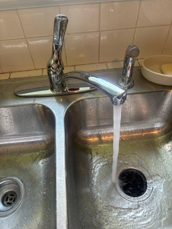 Installed customer-supplied chrome kitchen faucet with pull-down spray attachment on double-basin stainless steel sink. Completed installation, tested water flow and spray function to verify proper operation, and ensured all connections were secure with no leaks detected.