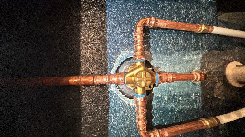 Installed customer-supplied shower valve assembly in bathtub enclosure. Completed all necessary plumbing connections using copper piping with soldered joints, integrated pressure regulator valve with gauge, and mounted chrome fixtures including single-handle control valve and tub spout with diverter. All components tested and operational upon completion.