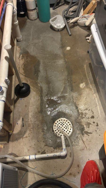 Responded to a backed-up floor drain in basement utility area. Upon arrival, found standing water pooled across concrete floor with significant accumulation around the drain assembly. Cleared blockage from the floor drain using mechanical augering methods, removed accumulated debris and sediment from drain basin, and verified proper water flow and drainage. Tested system to confirm complete restoration of drainage function.