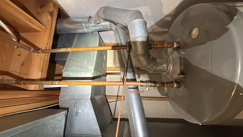 Responded to report of water heater leaking from the bottom in basement. Upon inspection, confirmed active leak at base of tanked water heater unit. Assessed unit condition and determined leak source from tank failure. Replaced failed water heater with new unit, ensuring proper connections to existing copper supply lines and galvanized piping assembly. Installed temperature and pressure relief valve, verified all connections for proper seal and function. Tested new water heater operation and confirmed no leaks present. Documented installation with photographs for service records.