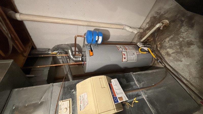 Completed installation of a 50-gallon gas-fired water heater in the utility room. Installed thermal expansion tank with proper copper piping connections and blue-handled shut-off valve at the water heater inlet. All connections were secured and tested for proper operation. The installation includes code-compliant venting with PVC exhaust piping and meets current safety standards with appropriate warning labels visible on the unit.