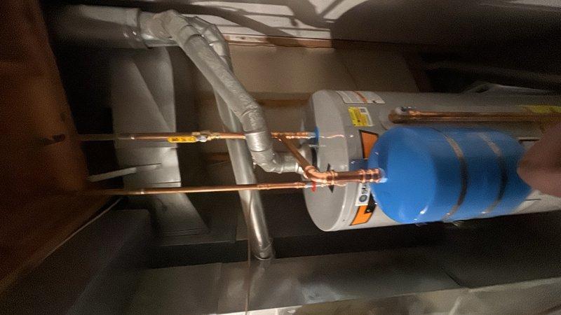Completed installation of a 50-gallon gas-fired water heater in the utility room. Installed thermal expansion tank with proper copper piping connections and blue-handled shut-off valve at the water heater inlet. All connections were secured and tested for proper operation. The installation includes code-compliant venting with PVC exhaust piping and meets current safety standards with appropriate warning labels visible on the unit.