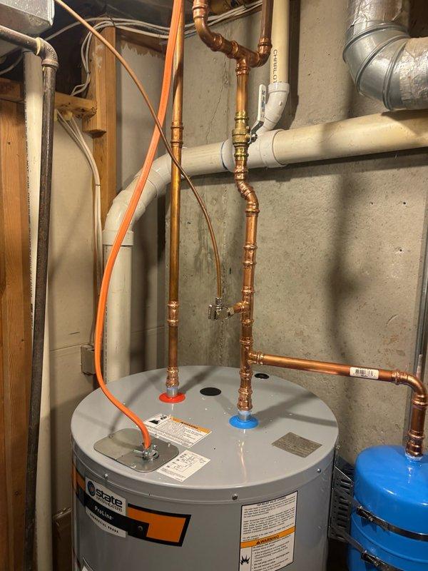 Installed a 50-gallon State brand electric water heater in basement utility area, utilizing a short configuration suitable for limited vertical clearance. Relocated the pressure reducing valve to the main water line and installed a new 3/4" ball valve on the main supply for improved system control. Added a blue thermal expansion tank mounted to the wall to protect against thermal expansion pressure buildup. Connected all hot and cold water supply lines using copper piping with brass fittings and shut-off valves, and installed temperature and pressure relief valve with discharge piping. Shut off water supply at the street to facilitate safe installation, then restored full water service and verified all connections for proper operation and absence of leaks.