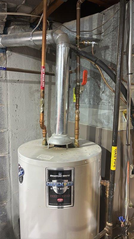 Conducted free estimate for replacement of 15+ year old 50-gallon gas water heater located in basement. Evaluated existing Bradford White Defender Safety System unit, which is currently operational but has exceeded recommended service life. Assessed installation configuration including copper supply lines with shut-off valves, galvanized vent piping, and connections to existing gas line. Photographed current water heater setup and surrounding mechanical room layout to prepare accurate replacement quote for 50-gallon gas unit with comparable specifications.