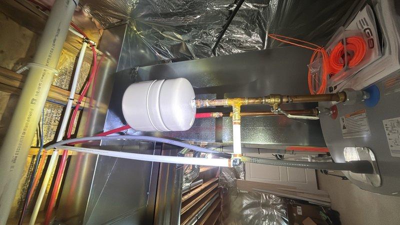 Completed plumbing maintenance inspection of residential HVAC air handler unit and water heater system. Inspected copper water supply lines with red and blue valve handles, verified proper brass fitting connections, and examined condensate reservoir assembly on air handler unit located in attic space. Evaluated water heater pressure relief valve assembly with WATTS pressure gauge reading 0-200 PSI range, confirmed proper mounting and fitting integrity at tank penetration point.