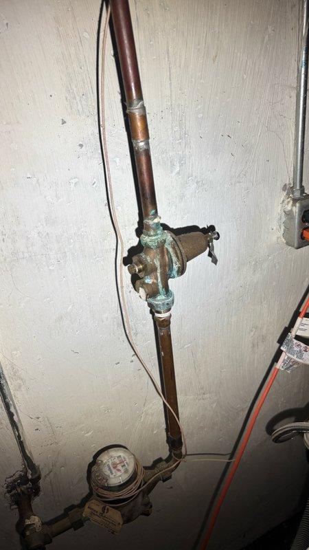 Responded to service call for low water pressure issue at residential property. Upon inspection, identified aging water meter and associated plumbing components as potential contributing factors to pressure concerns. Installed ProLine pressure gauge assembly with brass fittings and manual shutoff valve to monitor system pressure and facilitate diagnostics. Gauge installation included copper pipe connections and proper valve placement for accurate pressure readings. Documented existing conditions including water heater overflow valve actively leaking and requiring replacement. Photographed current plumbing configuration showing vertical copper supply line, existing meter assembly with visible wear and patina, and newly installed pressure monitoring equipment. Assessed water meter condition and determined replacement quotation needed due to age and deterioration of components. Provided customer with comprehensive evaluation of plumbing system status and recommended repair options for pre