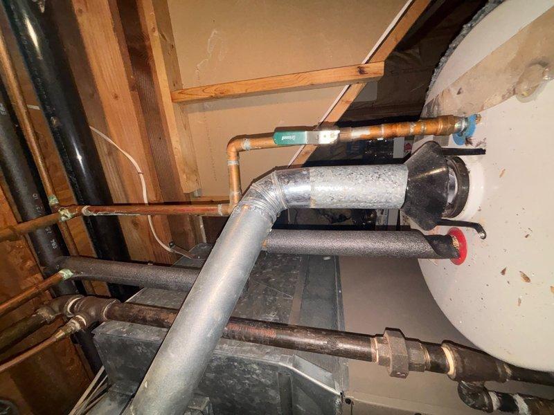 Responded to service call for non-functioning water heater replacement in basement. Upon arrival, assessed existing unit over 20 years old that had failed and was no longer operational. Inspected basement utility area, documenting existing plumbing configuration including copper supply lines, galvanized piping, and current water heater connections. Photographed existing installation showing aged copper pipes with oxidation, black insulated lines, ductwork, and wooden ceiling joists to document pre-existing conditions and plumbing layout. Observed moisture condensation on galvanized piping and various pipe connections throughout the utility space. Provided comprehensive estimate for complete water heater replacement including removal of old unit and installation of new system with proper connections to existing plumbing infrastructure.
