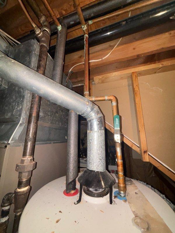 Responded to service call for non-functioning water heater replacement in basement. Upon arrival, assessed existing unit over 20 years old that had failed and was no longer operational. Inspected basement utility area, documenting existing plumbing configuration including copper supply lines, galvanized piping, and current water heater connections. Photographed existing installation showing aged copper pipes with oxidation, black insulated lines, ductwork, and wooden ceiling joists to document pre-existing conditions and plumbing layout. Observed moisture condensation on galvanized piping and various pipe connections throughout the utility space. Provided comprehensive estimate for complete water heater replacement including removal of old unit and installation of new system with proper connections to existing plumbing infrastructure.