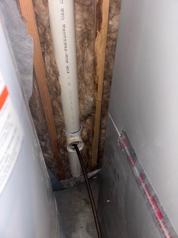Responded to reported kitchen sink backup causing flooding in multiple areas of the home. Upon investigation, discovered the issue extended beyond the kitchen sink to involve compromised drainage system components. Accessed wall cavity to inspect vertical drain stack and found deteriorated toilet flange with significant rust staining and moisture damage indicating long-term water exposure. The wax ring showed advanced age and deterioration, contributing to improper sealing and water escape. Removed damaged flange components and prepared substrate for replacement installation. Inspected vertical PVC drain pipe within wall cavity to ensure proper drainage flow and verified no additional blockages or structural concerns with the drain stack. Documented existing conditions including exposed framing, insulation, and drainage components. Addressed immediate drainage concerns and prepared system for necessary repairs to restore proper function and prevent further water damage to surrounding a