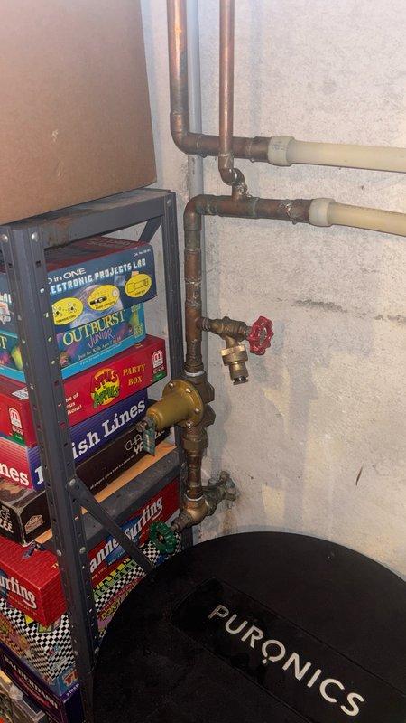 Performed scheduled maintenance service on Puronics water softening system located in basement utility area. Inspected system components including copper and brass piping connections, valve assemblies, and control mechanisms. Collected water samples in glass testing bottles to analyze water hardness levels and verify system performance. Checked red-handled isolation valve operation and examined all plumbing connections for proper function. System restored to optimal operating condition with all components functioning as designed.