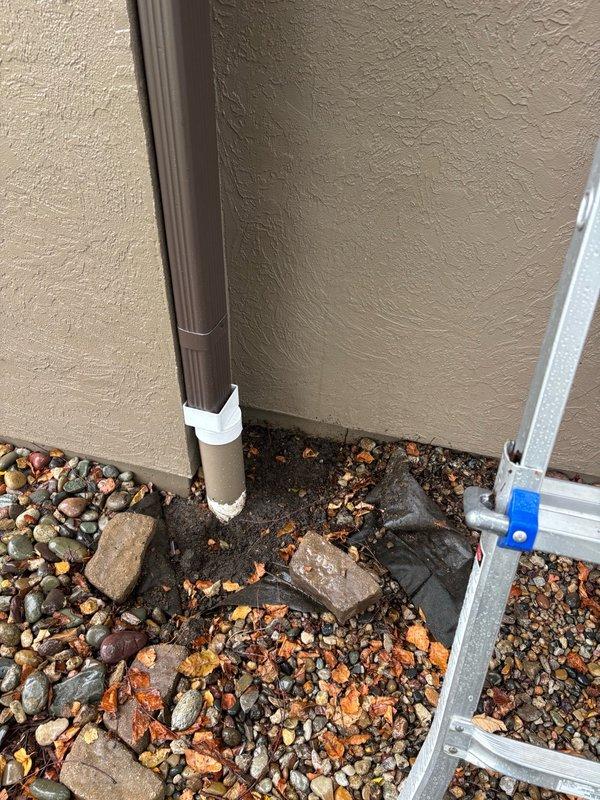 Responded to report of water dripping in basement originating from master bathroom area. Conducted thorough leak location inspection of affected areas including basement ceiling, HVAC system components, and exterior drainage systems. Investigated potential sources including plumbing fixtures, supply lines, and building envelope penetrations. Documented findings with photographic evidence showing HVAC ductwork, spray foam insulation at wall junctions, and exterior downspout drainage system with landscape rock bed at building foundation. Identified areas requiring further monitoring or repair to resolve moisture intrusion issue.