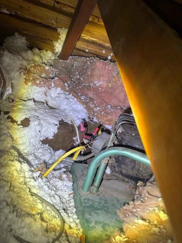 Responded to emergency water leak originating from attic space affecting multiple interior walls on split-level residence. Upon inspection, identified water heater as source of leak with water infiltrating through ceiling at four separate wall locations. Accessed attic crawl space to assess damage and locate primary leak point. Found water saturation in fiberglass insulation surrounding water heater area with evidence of mineral deposits on reflective insulation surfaces. Isolated water supply to water heater and addressed active leak. Documented extent of water damage to insulation materials and mechanical systems in attic space for insurance and repair purposes.