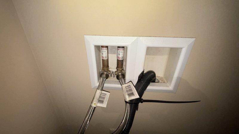 Completed comprehensive whole home plumbing inspection. Examined toilet tank components including flapper valve assembly with float mechanism, fill valve, overflow tube, and flush chain—all components found in functional condition with minor mineral deposits noted. Inspected ceiling-mounted plumbing access panel revealing organized installation of braided stainless steel water supply lines with shut-off valves and corrugated drain lines, all properly secured and accessible for future maintenance.