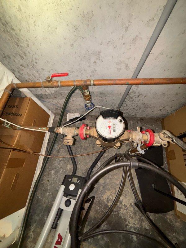 # Plumbing Maintenance Visit

Completed scheduled plumbing maintenance inspection of water meter assembly and associated piping system. Documented existing conditions including aged copper supply lines with oxidation, brass shut-off valves with red handles in operational position, and water meter with visible face readings. Observed significant ceiling moisture staining above plumbing installation indicating past water intrusion. Photographed corroded metal pipes and fittings showing advanced deterioration from long-term moisture exposure, along with bundled electrical cables secured beneath meter assembly. All components accessible and system currently functional at time of inspection.