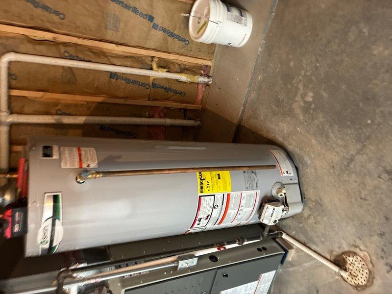 Responded to service call for intermittent water drip from pressure relief valve on tanked water heater in basement of 26-year-old residence. Upon inspection, examined all plumbing connections, copper piping, brass fittings, and pressure relief valve assembly mounted on the water heater. Found no active leaking at time of arrival, which is consistent with reported intermittent nature of the issue. Verified that minor weeping from temperature and pressure relief (TPR) valve can occur during normal thermal expansion cycles, particularly when water is heated and expands within the tank. Inspected expansion tank mounted on wall to confirm proper operation and air charge. Checked all visible plumbing connections including inlet and outlet pipes, valve assemblies, and mounting hardware for signs of deterioration or improper installation. Documented current condition of water heater installation with photographic evidence showing copper supply lines, brass fittings, blue-handled isolation val