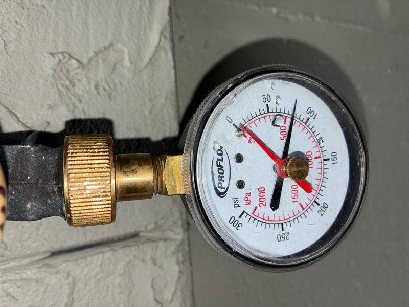 # Plumbing Inspection Report

Completed comprehensive whole home plumbing inspection including evaluation of water pressure, supply line connections, and shut-off valve functionality. Water pressure tested at 60-65 PSI using calibrated pressure gauge, confirming adequate system pressure within normal residential operating range. Inspected dual brass quarter-turn ball valves with blue handles serving appliance water supply lines, noting minor mineral deposits and tarnishing on valve bodies consistent with normal aging but no signs of active leaks or operational deficiencies. Verified proper installation of black corrugated flexible supply hoses with compression fittings and confirmed secure connections at all points. Examined copper pipe connections and mounting hardware, finding all components properly secured and functioning as intended with no immediate repair needs identified.