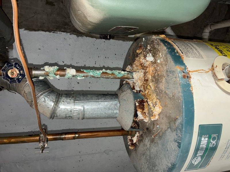 Responded to HVAC follow-up call for reported water heater leak. Upon arrival, performed comprehensive inspection of tanked water heater unit and surrounding plumbing components. Found extensive corrosion and deterioration throughout the system, including severe rust buildup on the water heater tank body, mounting bracket, and support structure. The teal-colored tank exterior showed significant paint failure with heavy oxidation underneath, indicating prolonged exposure to moisture and age-related degradation.

Documented heavy corrosion on copper supply piping with characteristic turquoise-green patina, as well as deterioration on galvanized steel piping connections. Identified white mineral deposits and crystalline buildup on pipe joints, suggesting ongoing leakage and mineral precipitation. The mounting hardware and bracket assembly displayed advanced rust with pitted surfaces and flaking metal, compromising structural integrity. Inspected associated expansion tank and pressure reli