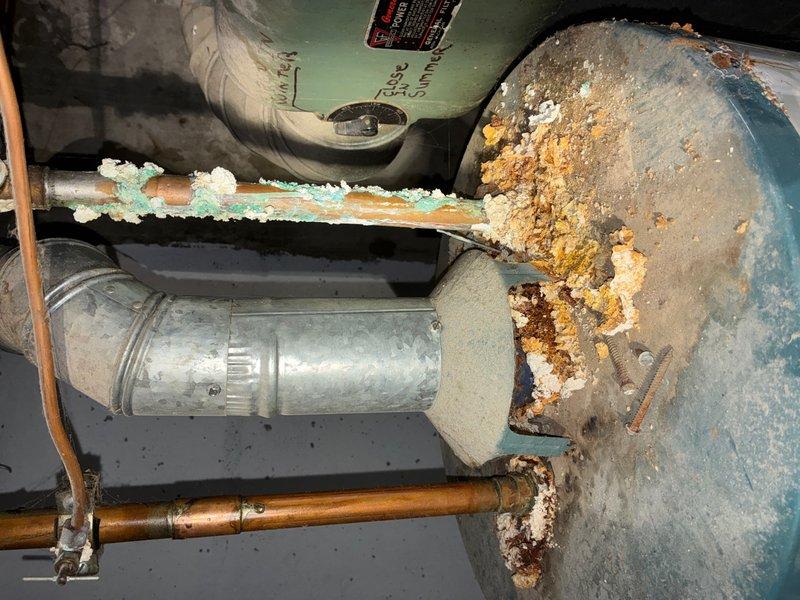 Responded to HVAC follow-up call for reported water heater leak. Upon arrival, performed comprehensive inspection of tanked water heater unit and surrounding plumbing components. Found extensive corrosion and deterioration throughout the system, including severe rust buildup on the water heater tank body, mounting bracket, and support structure. The teal-colored tank exterior showed significant paint failure with heavy oxidation underneath, indicating prolonged exposure to moisture and age-related degradation.

Documented heavy corrosion on copper supply piping with characteristic turquoise-green patina, as well as deterioration on galvanized steel piping connections. Identified white mineral deposits and crystalline buildup on pipe joints, suggesting ongoing leakage and mineral precipitation. The mounting hardware and bracket assembly displayed advanced rust with pitted surfaces and flaking metal, compromising structural integrity. Inspected associated expansion tank and pressure reli